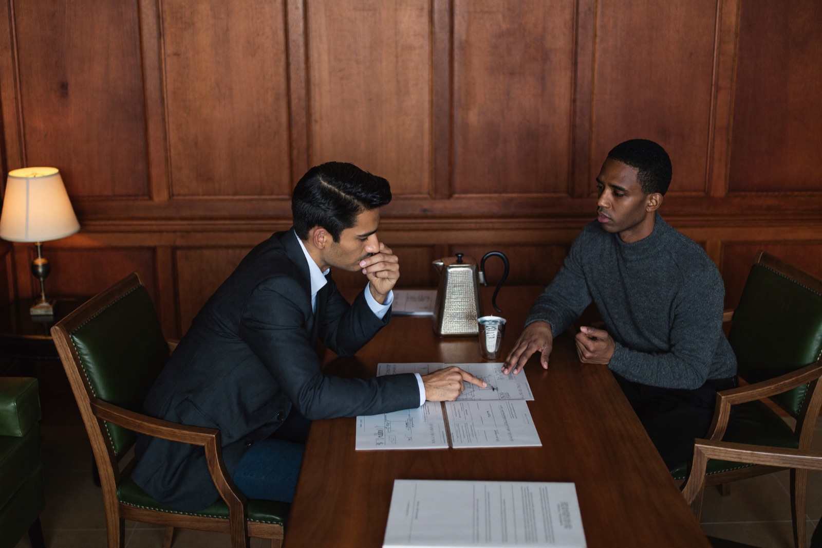 An advisor and a client reviewing property documents and floor plans at a walnut table in a wood-panelled study.