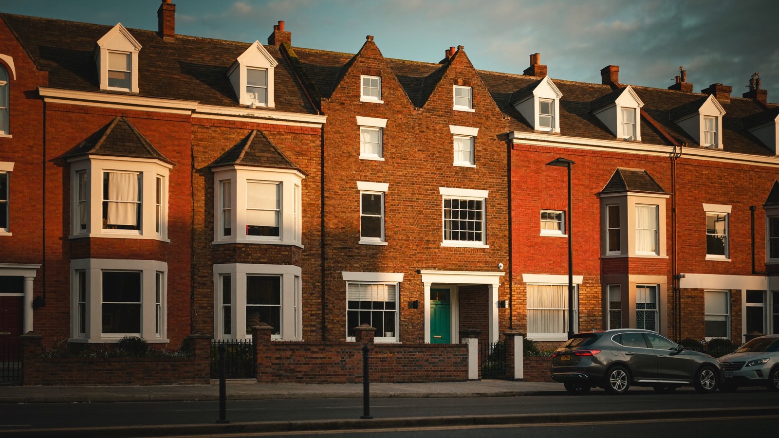 A street of Victorian red-brick terraced houses at golden hour, one with a racing-green front door.